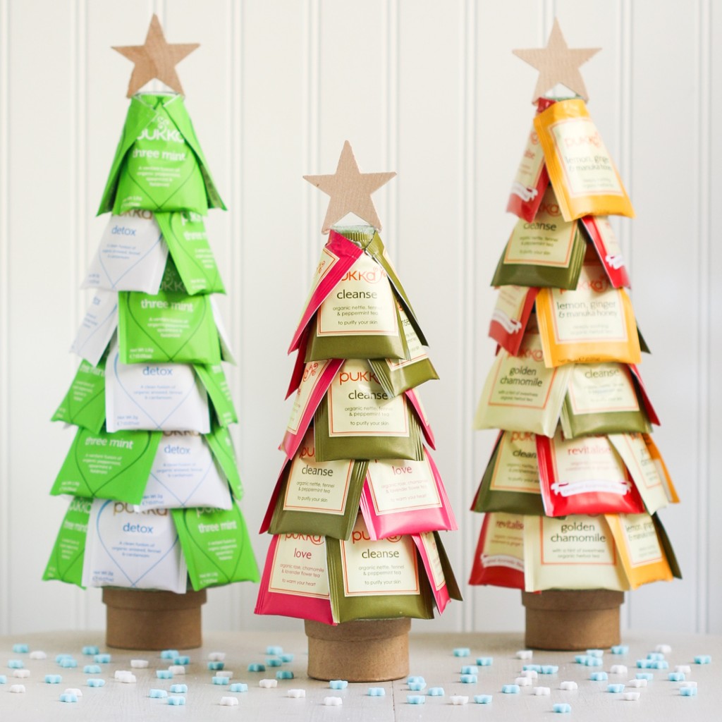 Three homemade mini christmas teas with green, white, pink and yellow teabags stuck on the side used as christmas tree branches and a gold paper star at the top of each tree.
